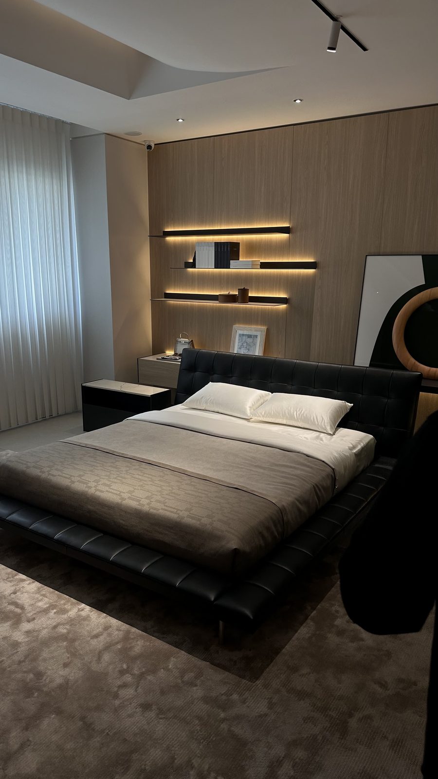 Bedroom with a black leather bed and backlit wooden shelving