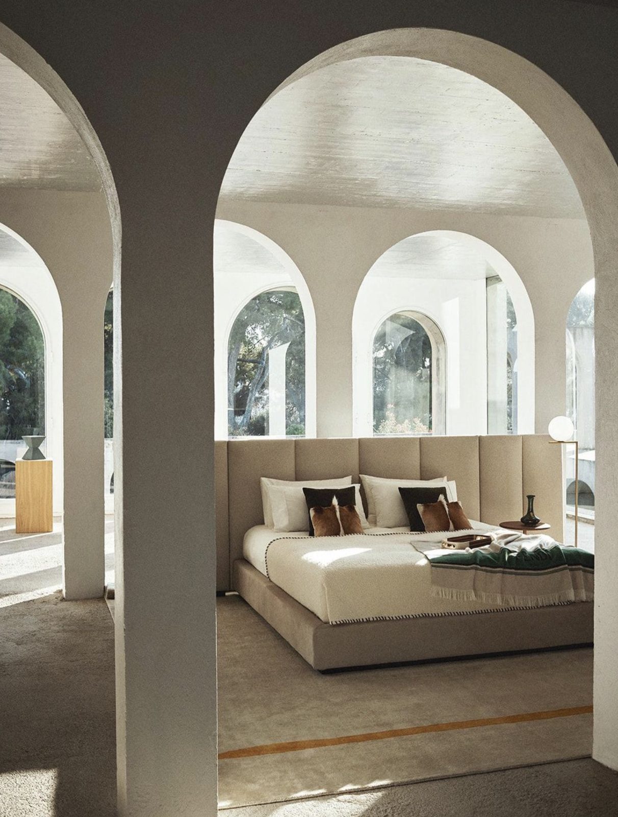 Upholstered bed with cushions and a throw under white arches
