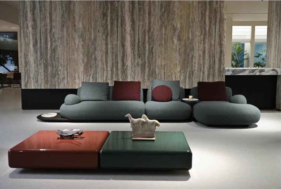 Salón con sofá verde, mesas lacadas y pared de travertino